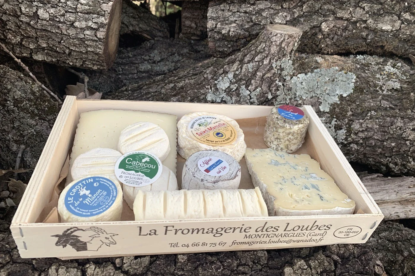 Un plateau de fromages dans une caisse en bois de la Fromagerie des Loubes, marquée de son estampille sanitaire.